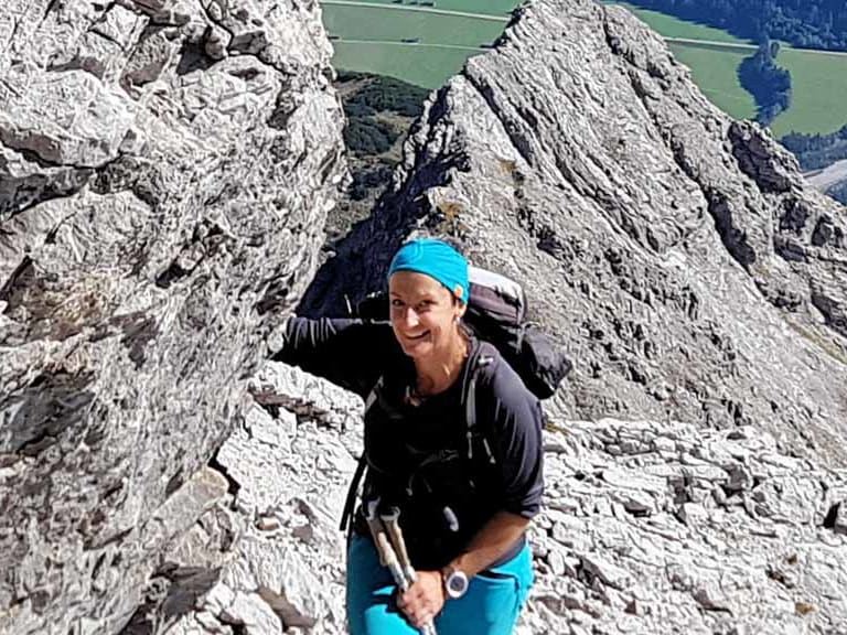 Bergwanderführerin Sabine Kühl mit türkisem Stirnband steigt über hellen Kalksteinschutt an einem steilen Felshang auf.