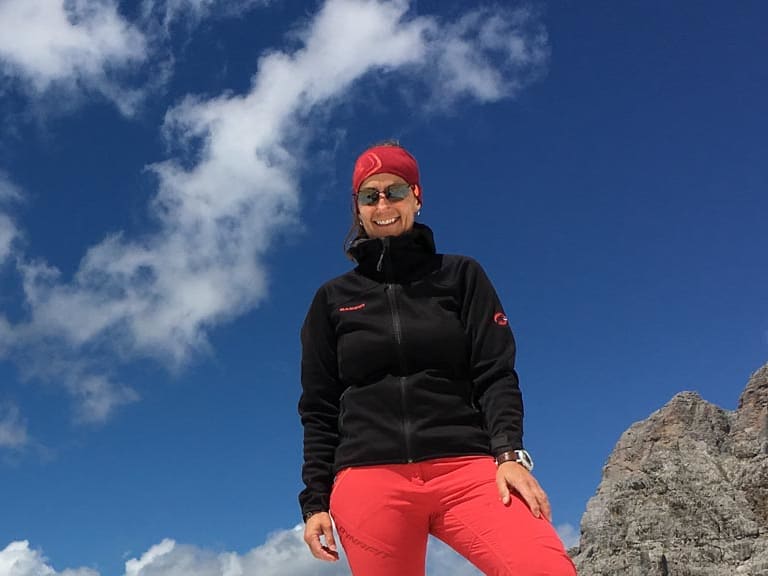 Bergwanderführerin Sabine Kühl steht auf einem Kalksteinfelsen am Watzmann mit Bergpanorama im Hintergrund.