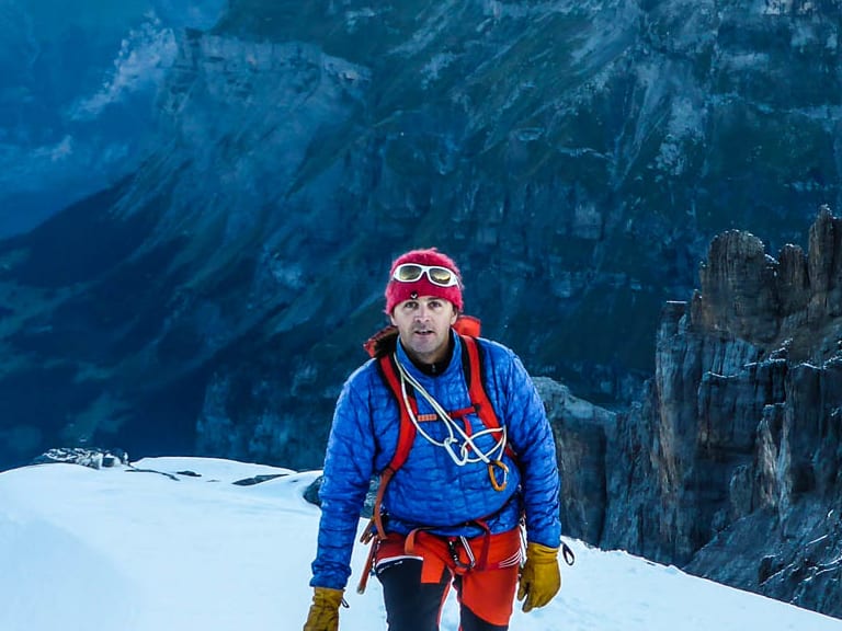 Auf einem schmalen Firnkamm am Ortler steht Bergführer Markus Hofmann mit Seil und Bergstock bei Morgenstimmung.