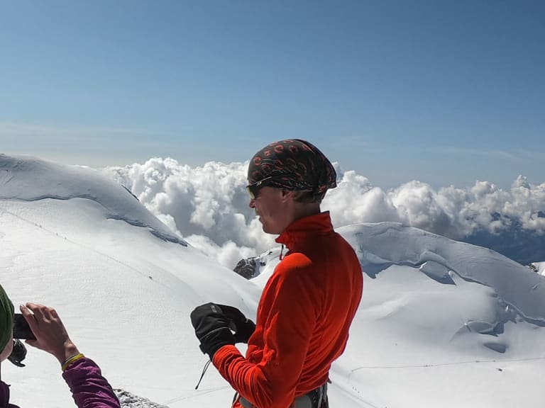 Drei Bergsteiger mit Bergführer Hubert Walther stehen auf verschneitem Gipfel oberhalb der Wolkendecke.