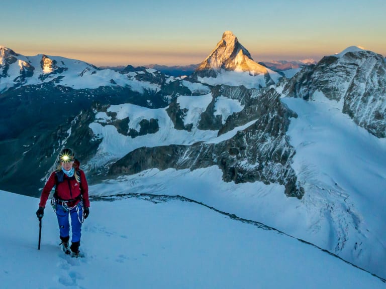 Bergwanderführerin Maria Müller steigt mit Helm, Eispickel und Steigeisen über spaltenreichen Gletscherboden auf.