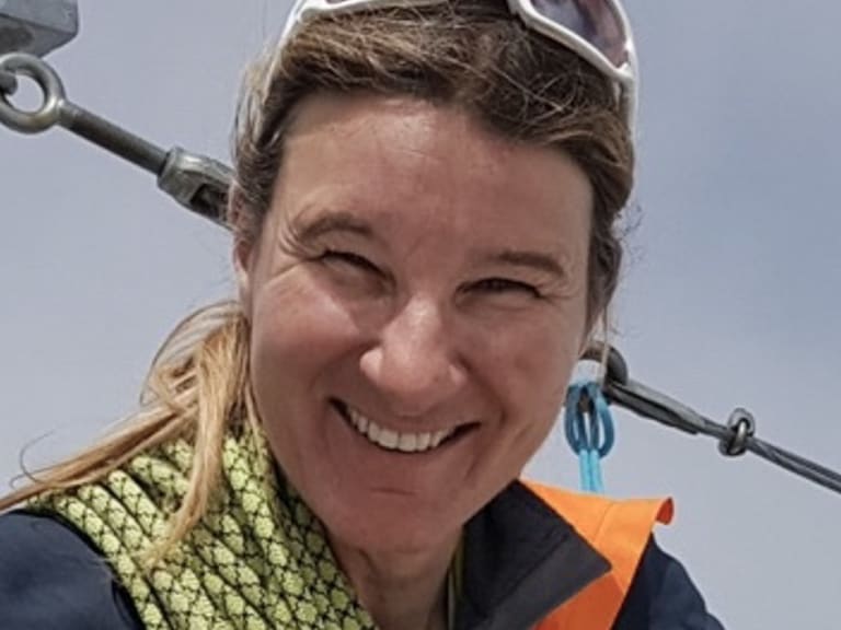 Bergwanderführerin Karin Toni Bigel lächelt freundlich vor einer Seilbahnkonstruktion und trägt ein gelbes Kletterseil um den Hals.