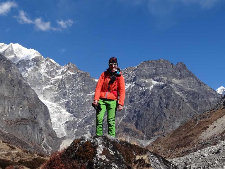 Bergwanderführerin Elisabeth Götzinger steht in orangener Jacke auf einem Felsbrocken im Hochtal.