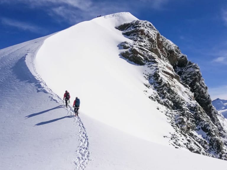 Bergführer Christian Färber steigt mit Begleitung auf schmalem Schneegrat in Richtung Gipfel mit Firnkappe auf.
