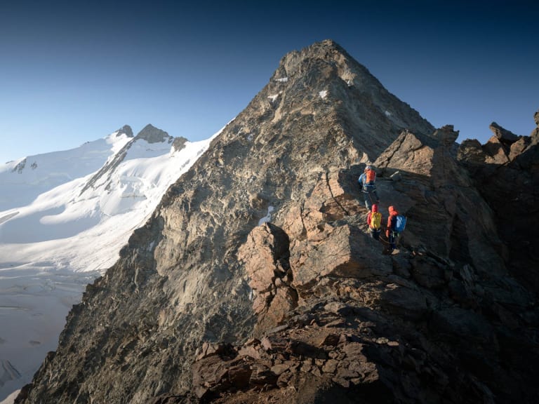 Auf einem schmalen Felsgrat bewegen sich drei Bergsteiger vorwärts, geführt von Bergführer Philipp Wagner.
