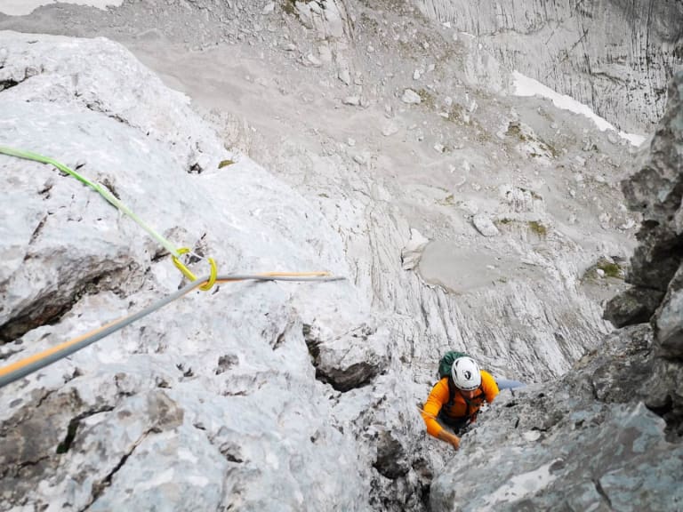 An grauem Kalksteinfels klettert Bergführer Philipp Wagner in orangefarbener Jacke durch eine Verschneidung aufwärts.