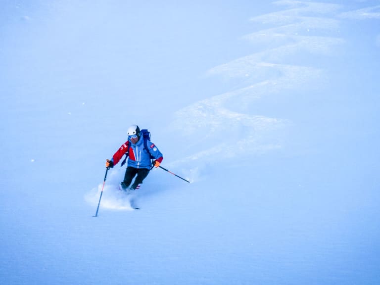 Bergführer Michael Eberharter fährt in roter Winterkleidung durch tiefen Pulverschnee, Schneewolke um die Skier.