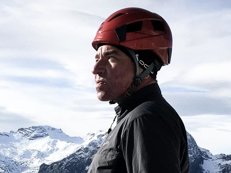 Bergwanderführer Helmut Freyer mit rotem Helm steht auf exponiertem Felsgrat über Wolkendecke im Winter.