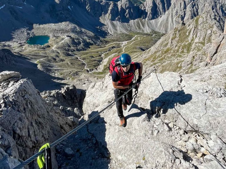 Aufnahme von oben zeigt Bergwanderführer Markus Radinger in roter Kleidung am steilen Kalkfels über türkisblauen Bergseen.