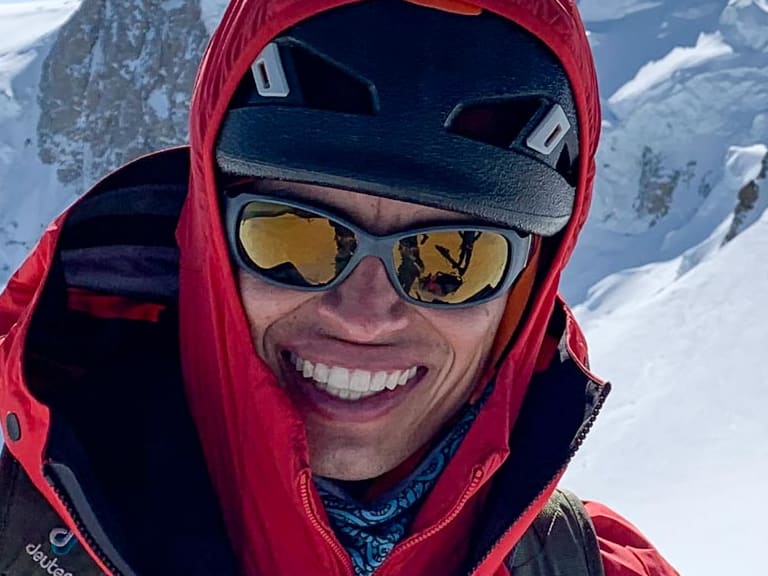 Portrait zeigt Bergführer José Salazar mit roter Kapuzenjacke und türkisfarben Kletterseil vor verschneiter Berglandschaft.