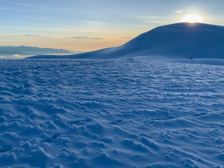 Weitläufige Schneefläche in Dämmerungsstimmung mit Bergführer José Salazar und Begleiter als kleine Figuren am rechten Bildrand.