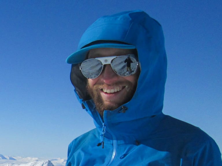 Bergwanderführer Bas Pijpers lächelt in blauer Hardshelljacke auf schneebedecktem Berggipfel mit Hochgebirgspanorama.
