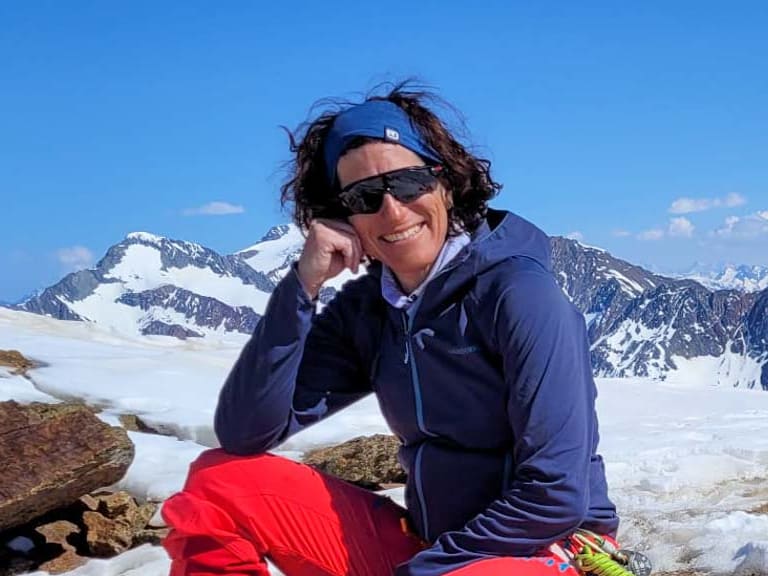 Bergwanderführerin Alexandra Querl sitzt entspannt auf einem Felsblock während einer Skitour in verschneiter Berglandschaft.