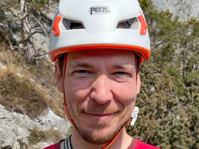 Bergführer Márk Salamon trägt weißen Petzl-Helm mit orangen Akzenten und lächelt in die Kamera.
