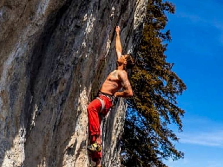 In roter Hose klettert Bergführer Tobias Riedlsperger an senkrechter Kalkstein-Wand über grünem Bergtal.