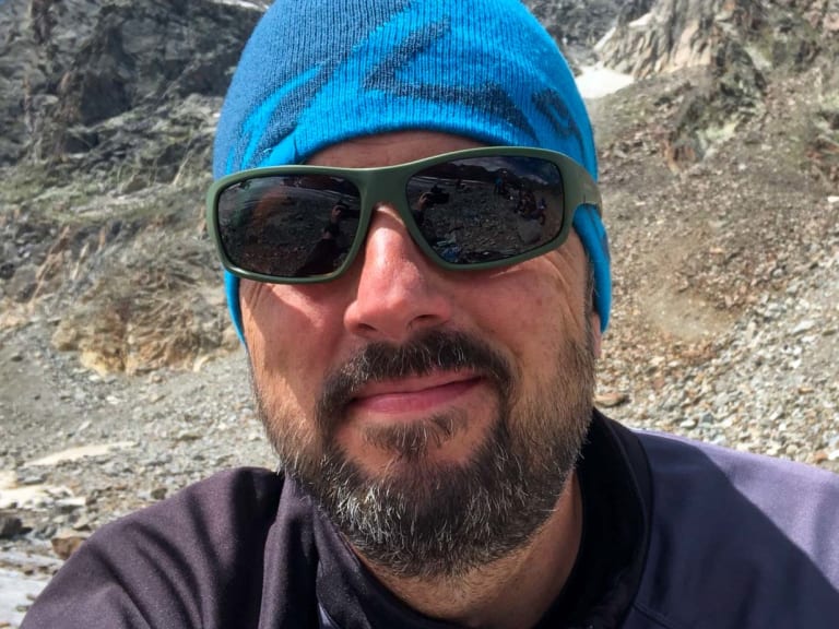 Mit blauer Strickmütze und Sonnenbrille steht Bergwanderführer Thomas Ziegler vor steilen grauen Felswänden.