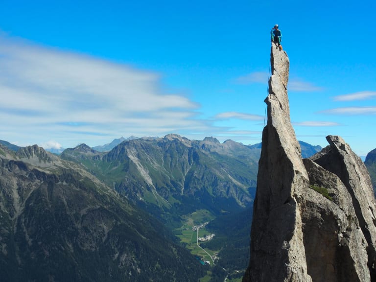 Bergführer Fabian Bendlin steht auf der Spitze einer hohen Felsnadel und blickt über Bergpanorama.