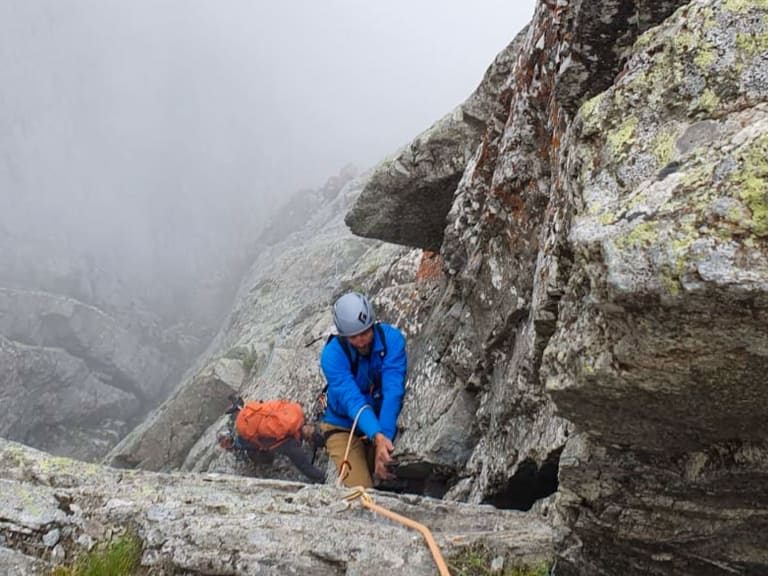 An einer steilen Felswand mit grauem Gestein klettert Bergführer Klaus Petz in blauer Jacke und weißem Helm.