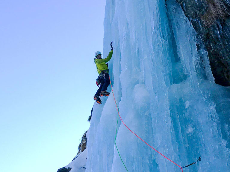 Bergführer Klaus Karlstätter klettert in gelber Jacke mit Eispickel und Steigeisen an einer blauen Eiswand, gesichert am rot-grünen Seil.
