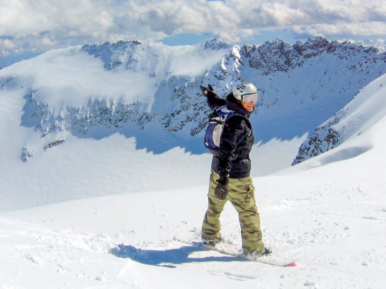 Im verschneiten Hochgebirge steht Bergführer Markus Arzberger auf einem Snowboard und blickt zu den schneebedeckten Gipfeln.