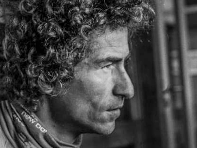 Schwarz-weiß Portrait zeigt Bergführer Alessandro Lucchi mit lockigem Haar im Profil, er trägt Outdoor-Bekleidung in Innenraum.