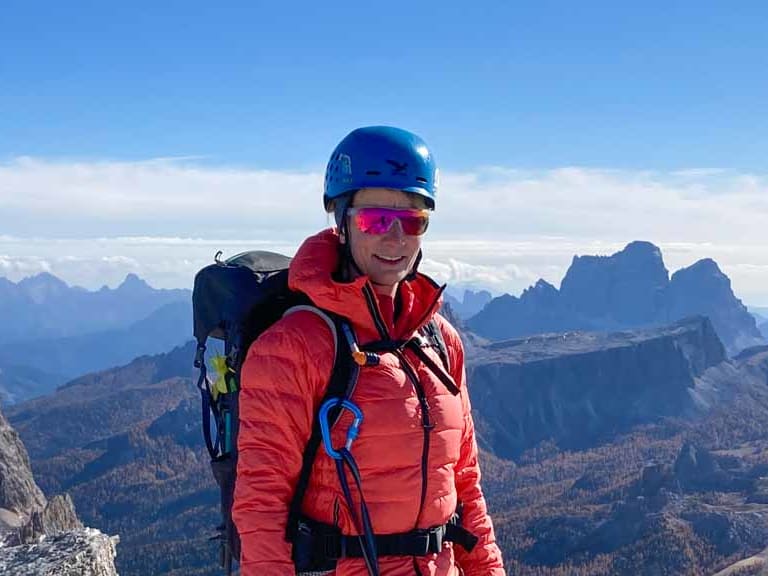 Bergwanderführerin Stefanie Erdmann steht mit blauem Helm und Klettersteig-Set auf Dolomitengipfel.