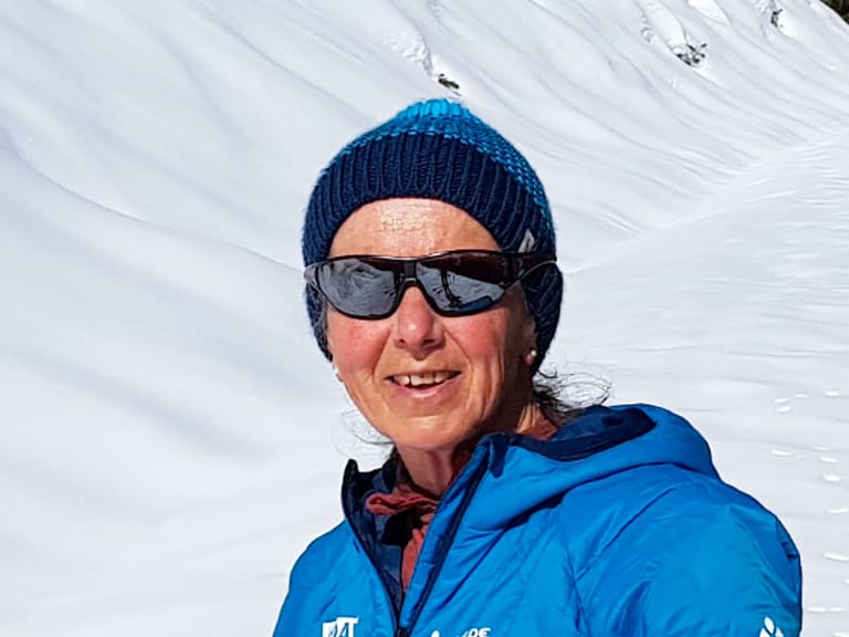 Bergwanderführerin Julia Riedl trägt blaue Winterjacke und Sonnenbrille vor verschneiter Berglandschaft im Winter.