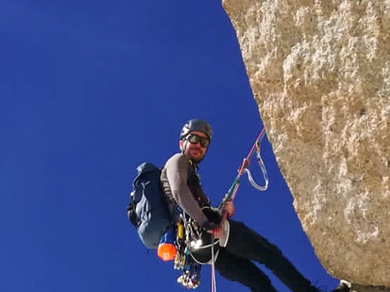 Mit Helm und Klettergurt hängt Bergführer Lukas Höllrigl am roten Seil an einer senkrechten Kalksteinwand.