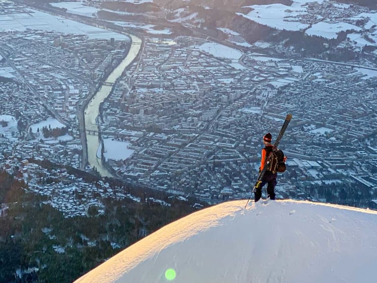Bergführer Lukas Höllrigl steht auf verschneitem Hang und blickt auf die ausgedehnte Stadtlandschaft im Tal hinab.