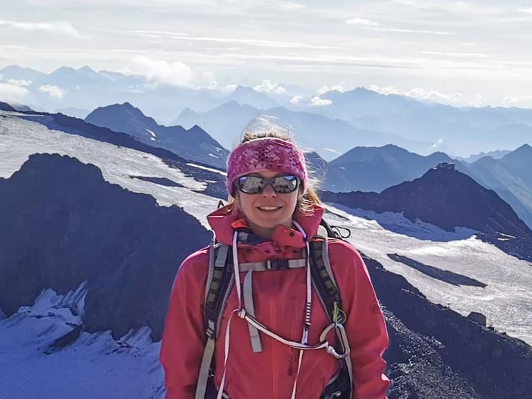 Auf einem Felsgrat steht Bergwanderführerin Patricia Neumair lächelnd vor einer weiten Gletscherlandschaft mit Spalten.