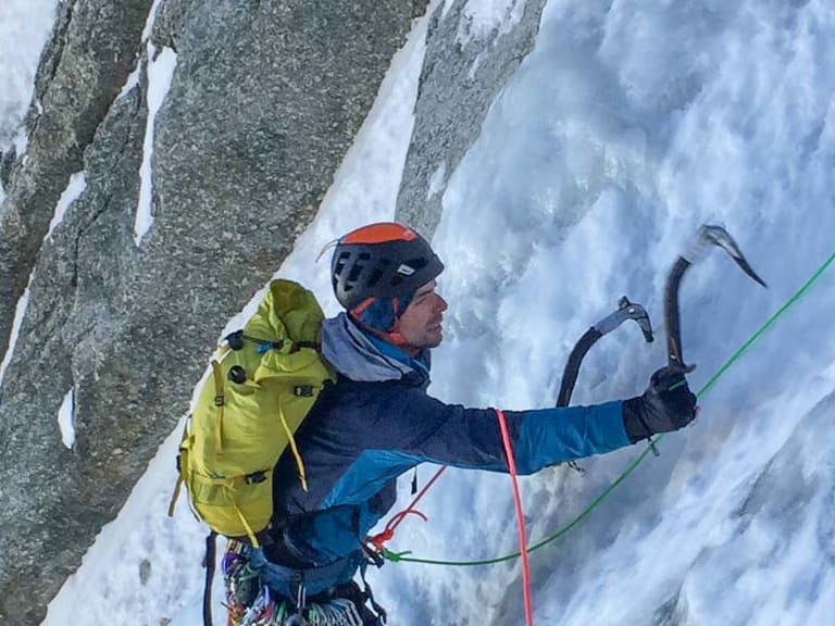 Bergführer Lukas Seedoch klettert mit zwei Eisgeräten an einer strukturierten Eiswand, gesichert über grünes Kletterseil.