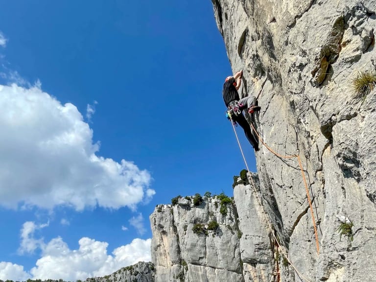 An heller Kalksteinwand klettert Jakob Fink als Bergführer aufwärts, mit Helm und orangem Kletterseil gesichert.