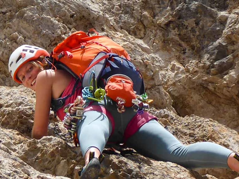 An steiler Kalksteinwand klettert Bergwanderführerin Anna Biller mit rotem Helm und Kletterausrüstung am Klettergurt.