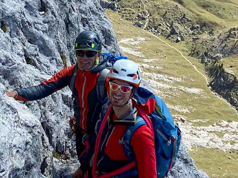 Bergführer Alexander Reisenhofer klettert mit Partner an steiler Kalksteinwand über grünen Almhängen.