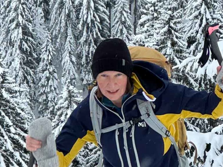 Bergwanderführerin Anna Schärtel bewegt sich mit Schneeschuhen und rosa Stöcken durch verschneiten Nadelwald.