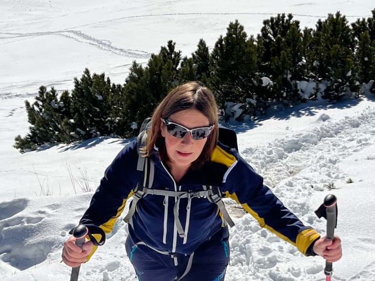 Mit roten Wanderstöcken steigt Bergwanderführerin Anna Schärtel durch tiefen Schnee bergauf in verschneiter Berglandschaft.