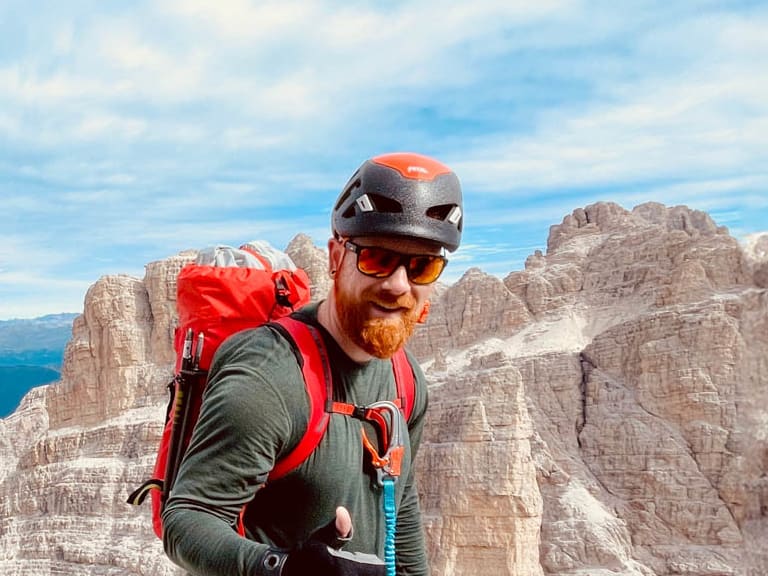 Bergwanderführer Dennis Enders steht mit Kletterausrüstung auf Felsplateau in den Dolomiten mit Panoramablick.