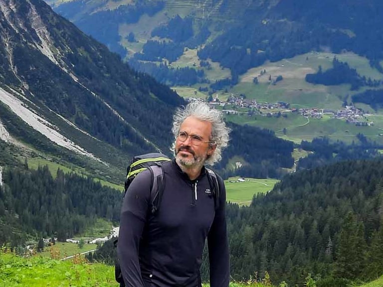 Auf grüner Almwiese in den Picos de Europa steht Bergwanderführer Nacho Carreras Codina mit Rucksack.