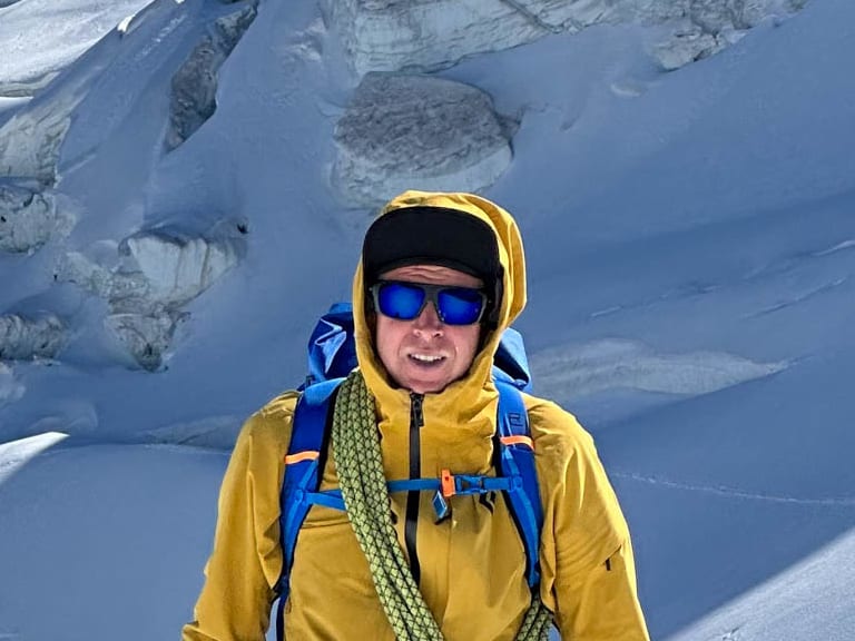 Bergführer Stefan Scheiblauer in gelber Bergjacke mit Eispickel und Kletterausrüstung vor zerklüfteter Gletscherlandschaft.