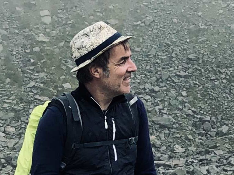 Bergwanderführer Alexander Hoffmann - Kuhnt mit hellem Hut sitzt lächelnd auf Felsblock in alpiner Gerölllandschaft.