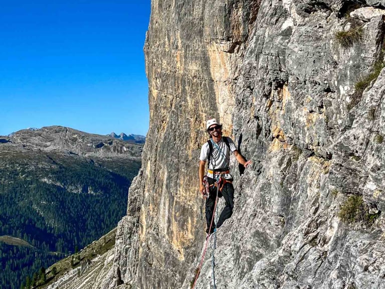 Bergführer Jakob Halder steht auf schmalem Felsband in steiler Kalksteinwand mit Klettergurt und rotem Seil.