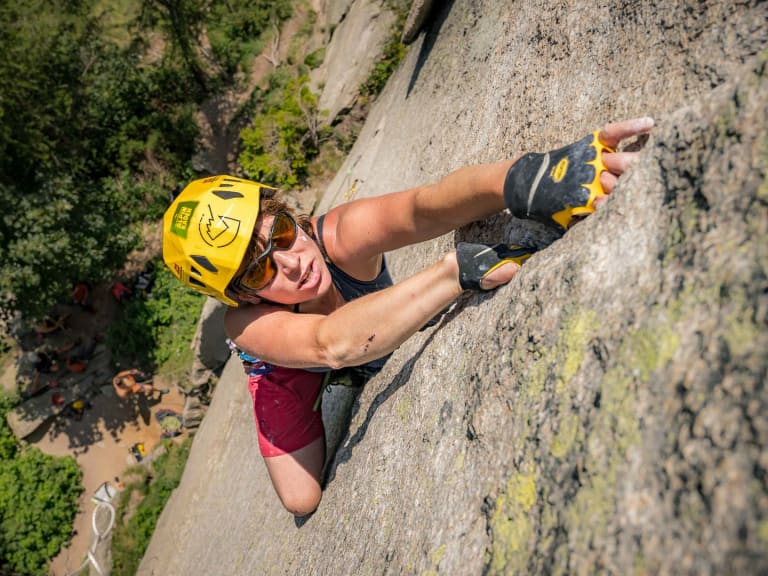 Mit gelbem Helm und Sonnenbrille klettert Bergführerin Tanja Kuster frei an senkrechter grauer Felswand.