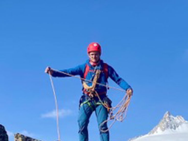 Bergführer Maurits Bakker steht mit Kletterseil auf einem schmalen Felsgrat vor schneebedeckten Gipfeln und Gletscherfeld.