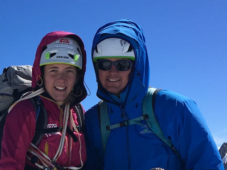 Zwei Personen stehen auf Felsgrat, rechts Bergwanderführer Patrick Hindelang in blauer Jacke mit Helm und Sonnenbrille.