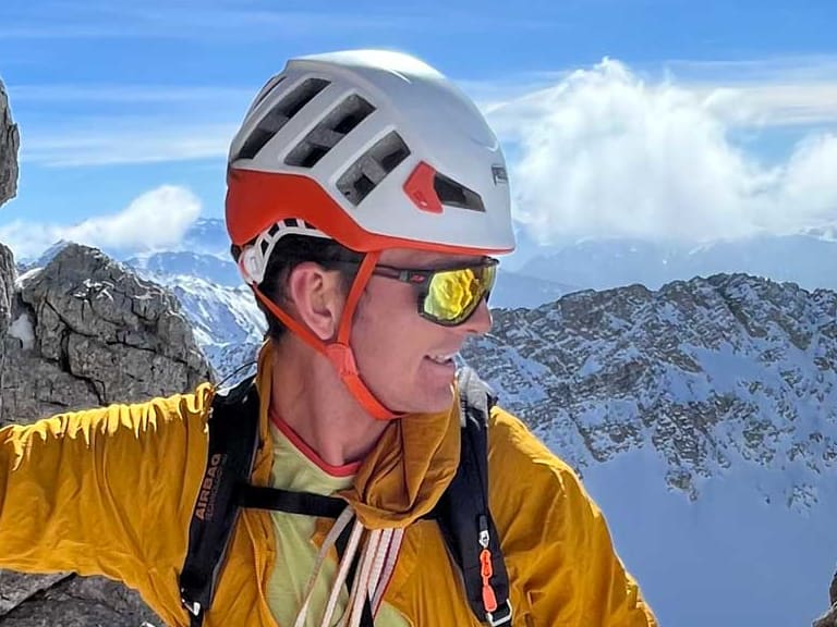 Bergwanderführer Patrick Hindelang klettert in gelber Softshell-Jacke an grauer Kalksteinwand mit weißem Helm und Klettergurt.