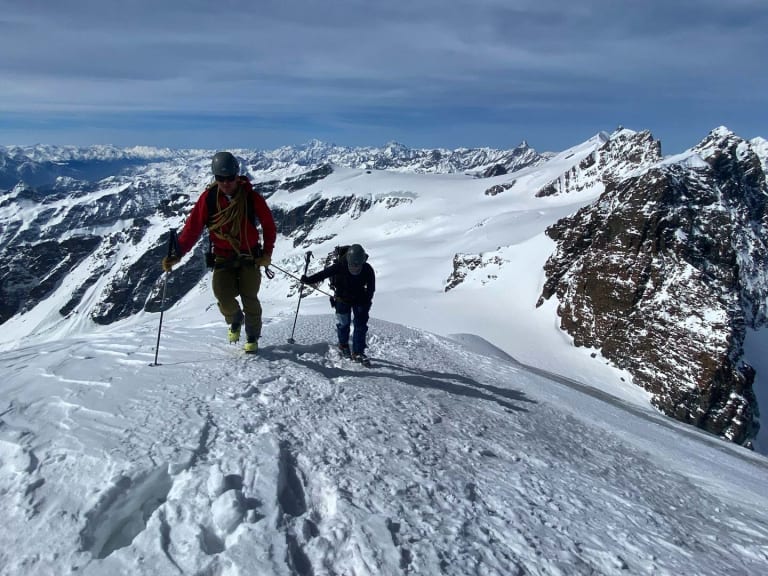 Zwei Personen gehen auf verschneitem Grat aufwärts, Bergführer Robert Kadner führt die Hochtour mit Helm und Bergstöcken.