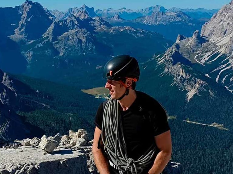 Bergführer Stephan Ulz steht auf einem Gipfelplateau aus hellem Kalkstein und hält ein aufgerolltes Seil in den Händen.