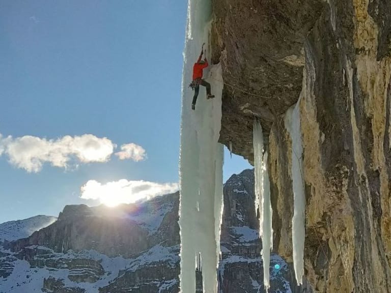An einer senkrechten Eiswand mit dicken Eiszapfen klettert Bergführerin Luca Trubbiani in roter Winterjacke.