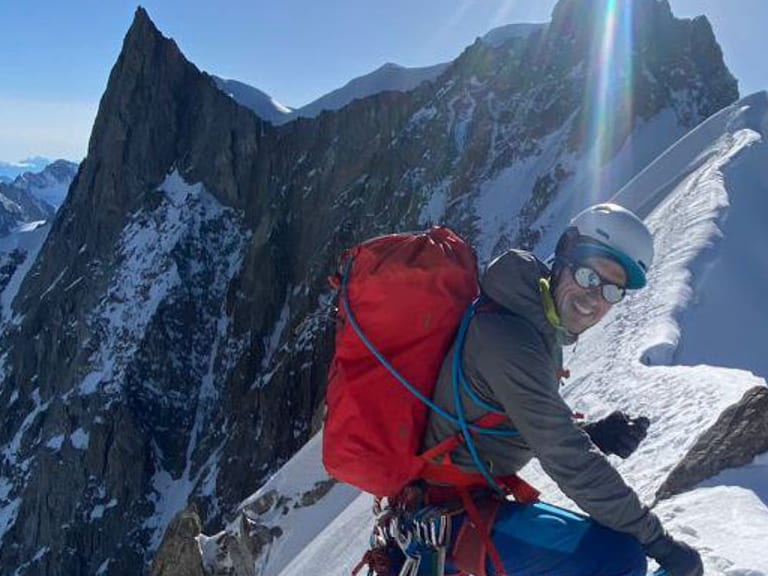 Bergführerin Luca Trubbiani bewegt sich auf einem schmalen, verschneiten Grat mit rotem Rucksack und Kletterausrüstung.
