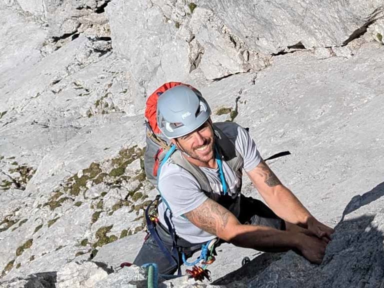 Von oben fotografiert klettert Bergführer Stefan Saller an heller Kalksteinwand und trägt weiß-roten Kletterhelm.